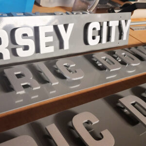 Flat Cut Metal letters assembled on wayfinding signage in busy downtown street. 