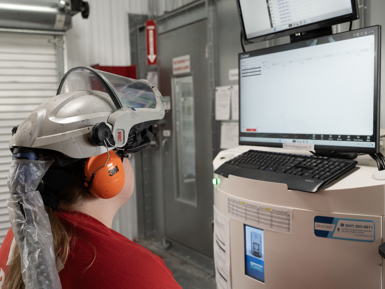 Team members engaged. An industry professional wearing safety gear engages with a digital workstation, learning a new skill in a manufacturing environment.